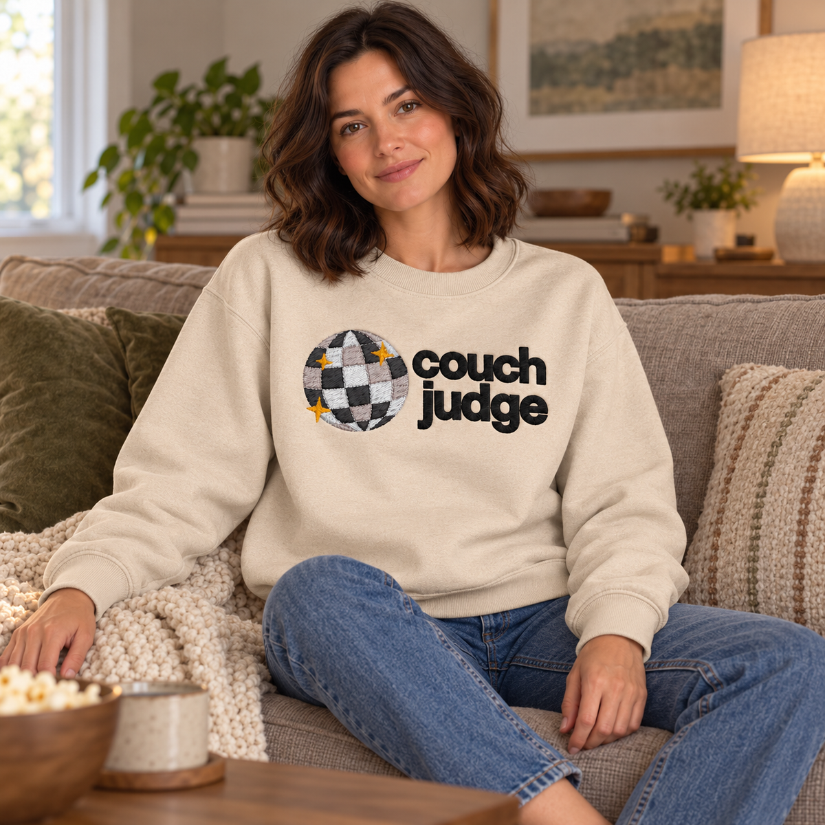 Same model wearing Sand crewneck on a sofa
